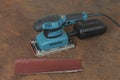 Electric sheet finishing sander and three abrasive papers on old rusty metal sheet., on background oriented strand board