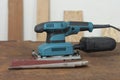 Electric sheet finishing sander and three abrasive papers on old rusty metal sheet., on background oriented strand board