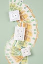 Electric sockets with Euro banknotes on light green background. Electricity cost and expensive energy concept. Top view Royalty Free Stock Photo