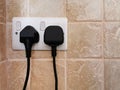 Electric sockets with two black electric plugs on tile wall.