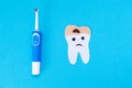 An electric toothbrush and a tooth cut out of felt, affected by caries. Blue background. Flat lay. The concept of modern dental Royalty Free Stock Photo