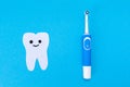 Electric toothbrush, toothpaste, a tooth carved out of felt with a smiling cartoon face. Blue background. Flat lay. The Royalty Free Stock Photo