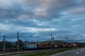 Electric train carrying wheat passing near a road on an overcast day