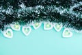 Electric white garland with glowing lights in the form of hearts and Christmas tinsel on turquoise background. Place for your text Royalty Free Stock Photo