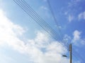 Electric wooden pole with lamp and electricity cables against blue sky and white clouds. Royalty Free Stock Photo