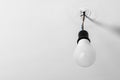 Electrical energy saving light bulb in black chuck hanging on colored wires on a white rough uneven ceiling Royalty Free Stock Photo