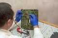 Electrical engineer uses multimeter to measure resistance on green printed circuit board at service center. LCD monitor repair.