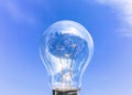 Electrical light bulb in hand on blue sky background. Hand holding light bulb on a background sky and sun. Royalty Free Stock Photo