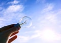 Electrical light bulb in hand on blue sky background. Hand holding light bulb on a background sky and sun. Royalty Free Stock Photo