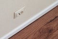 Electrical outlet on beige home wall with wallpaper, white baseboard and brown wooden laminate Royalty Free Stock Photo