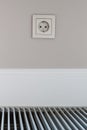 Electrical outlet located on wall above white wooden skirting Board and convector built into the floor