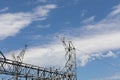 Electrical power lines entering a power transfer station, gridded trusses against a blue sky with clouds Royalty Free Stock Photo