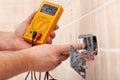 Electrician hands checking voltage in a partially mounted electrical socket - closeup