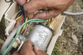 An electrician inspects the wiring connected to CBB65A-1 capacitor inside a window type air conditioner control panel outside Royalty Free Stock Photo