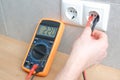 The electrician measures the voltage in the home network by inserting a voltmeter into the outlet. Close-up view of the hands with