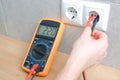 The electrician measures the voltage in the home network by inserting a voltmeter into the outlet. Close-up view of the hands with Royalty Free Stock Photo