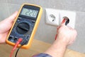 The electrician measures the voltage in the home network by inserting a voltmeter into the outlet. Close-up view of the hands with Royalty Free Stock Photo
