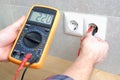 The electrician measures the voltage in the home network by inserting a voltmeter into the outlet. Close-up view of the hands with
