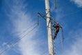 An electrician in an orange helmet climbs a high voltage power tower