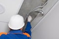 Electrician in a protective helmet, fixes a malfunction in communications hidden in the suspended ceiling, close-up