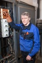 Electrician repairman in blue uniform standing near high voltage industrial panel