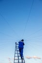 Electrician repairs electrical wiring on the roof of a high-rise building standing on the stairs against the blue sky.