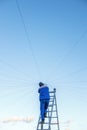 Electrician repairs electrical wiring on the roof of a high-rise building standing on the stairs against the blue sky. Royalty Free Stock Photo