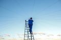 Electrician repairs electrical wiring on the roof of a high-rise building standing on the stairs against the blue sky. Royalty Free Stock Photo