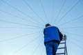 Electrician repairs electrical wiring on the roof of a high-rise building standing on the stairs against the blue sky. Royalty Free Stock Photo