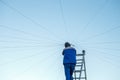 Electrician repairs electrical wiring on the roof of a high-rise building standing on the stairs against the blue sky. Royalty Free Stock Photo