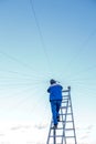 Electrician repairs electrical wiring on the roof of a high-rise building standing on the stairs against the blue sky. Royalty Free Stock Photo