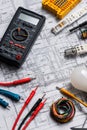 Electrician's toolkit: multimeter, wires, light bulb, and blueprints on a desk Royalty Free Stock Photo
