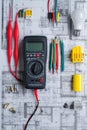 Electrician's toolkit: multimeter, wires, light bulb, and blueprints on a desk Royalty Free Stock Photo