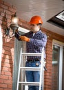 Electrician standing on ladder and changing outdoor lamp Royalty Free Stock Photo