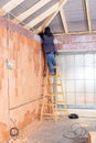 Electrician standing on ladder installing cables in the channel / groove along with electrical boxes in unfinished house.