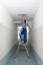 Electrician on stepladder installs lighting to the ceiling