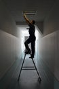Electrician on stepladder installs lighting to the ceiling