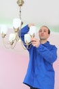 Electrician twists bulb in the chandelier on the Royalty Free Stock Photo