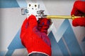 An electrician wearing red protective gloves uses a screwdriver to install a socket into the wall of the living room. Close-up of Royalty Free Stock Photo