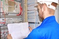 Electrician in white helmet is looking at electrical diagram in control cabinet of industrial equipment.