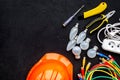 Electrician work concept. Hard hat, tools, cabel, bulb, socket outlet on black background top view space for text Royalty Free Stock Photo