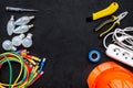 Electrician work concept. Hard hat, tools, cabel, bulb, socket outlet on black background top view space for text Royalty Free Stock Photo