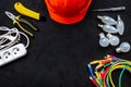 Electrician work concept. Hard hat, tools, cabel, bulb, socket outlet on black background top view space for text Royalty Free Stock Photo