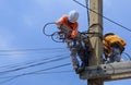 Electricians with safety equipment are working to install electrical system on power pole against blue sky background