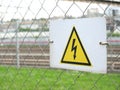 Electricity caution sign on trellised fence, on blurred city background, danger sign Royalty Free Stock Photo