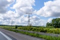 High voltage power line pylons, electrical tower on a green field with blue sky. Highway with cars on a cloudy summer day Royalty Free Stock Photo