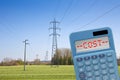Electricity costs concept with power tower, transmission lines and calculator with cost text against a rural scene Royalty Free Stock Photo