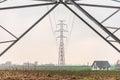 High voltage overhead power line, power pylon, steel lattice tower standing in the field. Small house. Royalty Free Stock Photo