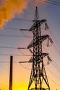 Electricity pylons against orange and yellow sunset. Energy distribution network. Selective focus. Royalty Free Stock Photo