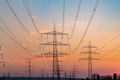 Electricity pylons and electric power transmission lines against vibrant orange sky at sunset. High Voltage towers provide power. Royalty Free Stock Photo